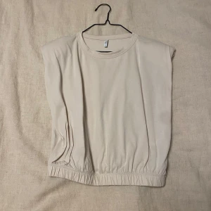 Beige ärmlös topp från Only - Säljer en stilren beige ärmlös topp från Only. Den har en elastisk nederkant som ger en snygg passform. Perfekt för både vardag och festliga tillfällen. Toppen är i mycket bra skick och gjord av mjukt material för extra komfort.
