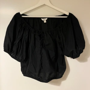 Svart topp från H&M - Svart topp från H&M i linneblandning. Toppen har korta puffärmar och en elastisk kant vid hals och midja för en bekväm passform. Toppen är oanvänd. 