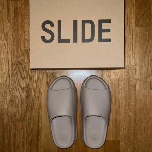 Adidas Yeezy Slide i beige - Säljer ett par stilrena Adidas Yeezy Slide i beige. Dessa är grymt sköna men säljer då ja inte använder dom. Tofflorna är använda 4-5 gånger. 