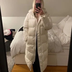 Vit lång dunjacka med huva - Säljer en vit dunjacka från vero Moda i strl 34, passar S/M också! Köpt förra året för 1000kr. Lite smutsig vid armarna och längst ner men går lätt att tvätta! 💕