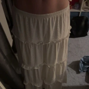 Vit långkjol med volanger - Säljer en vit långkjol med flera lager av volanger. Kjolen har en luftig och flödande design. Den är idealisk för varmare väder och ger en elegant touch till din outfit. Använd fåtal gånger, skriv för mer information💕