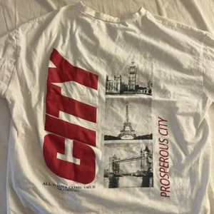 T shirt - Vit t-shirt med tryck på baksidan. Trycket visar en bild av Big Ben, Eiffeltornet och Tower Bridge med texten "CITY" och "PROSPEROUS CITY". Säljs 100