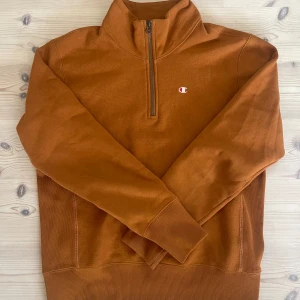 Orange tröja från Champion - Säljer en snygg orange tröja från Champion i storlek medium. Den har en halv dragkedja framtill och är perfekt för höst och vinter. Tröjan är i bra skick och har en mysig insida som håller dig varm. Perfekt för vardagsbruk eller en avslappnad dag ute.