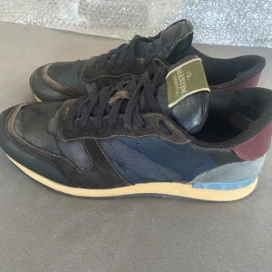 Valentino sneakers i flera färger - Säljer ett par snygga Valentino Rockrunners. De har en bas i svart och blått med detaljer i vinrött och grått. Skorna har en klassisk snörning och en bekväm sula som är perfekt för vardagsbruk.  