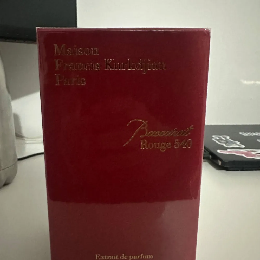 Säljer en lyxig parfym från Maison Francis Kurkdjian, Baccarat Rouge 540 Extrait de Parfum. Förpackningen är elegant i en djup röd färg med guldtext och detaljer. Den har en stilren design med en bild av en byggnad på sidan. Perfekt för den som vill ha en exklusiv doftupplevelse.. Parfym.