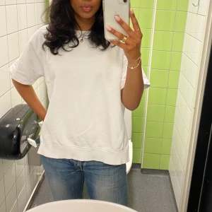 Vit t-shirt - Säljer en enkel och stilren vit t-shirt. Den har en normal passform och korta ärmar, perfekt för vardagsbruk. T-shirten är i bomull och känns skön mot huden. Passar till allt och är ett måste i garderoben!
