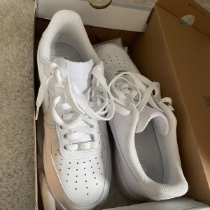 Vita Nike Air Force 1 sneakers - Säljer ett par klassiska vita Nike Air Force 1 sneakers i nyskick. De är helt vita med snörning och har den ikoniska perforerade tån för ventilation. Skorna är i storlek 42,5 och kvitto finns. Perfekta för både vardag och styling. Mvh 