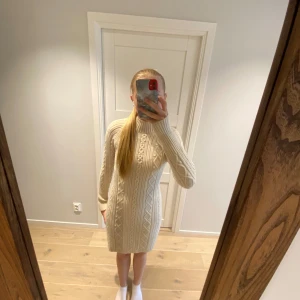 Beige stickad klänning från Zara - Säljer en superfin beige stickad klänning från Zara. Den har ett snyggt flätmönster och är perfekt för höst och vinter. Klänningen är långärmad och har en normal passform, vilket gör den både bekväm och stilren. Perfekt för mysiga dagar eller en avslappnad fest! Helt ny