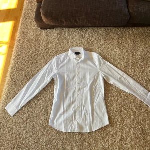 Vit skjorta från Riley - Säljer en klassisk vit skjorta från Riley. Den är långärmad och har en stilren design med knappar framtill. Perfekt för både formella och avslappnade tillfällen. Skjortan är i nyskick och gjord av ett bekvämt material. Storlek: M (slim fit)