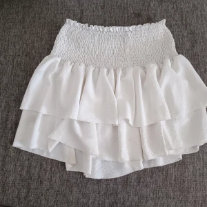 Vit volangkjol - Säljer en superfin vit kjol med volanger. Den har en elastisk midja som gör den bekväm och lätt att bära. Perfekt för sommaren. Kjolen är kort och har en luftig 🤍 obs betalning bara Swish 