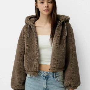 Brun teddyjacka med huva - Mysig brun teddyjacka med huva, perfekt för kyliga dagar. Jackan har en croppad passform och långa ärmar. Den är gjord av mjukt teddy-material och har en dragkedja framtill. Perfekt för höst och vinter!