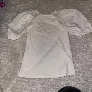 Vit topp med puffärmar - Säljer en söt vit topp med puffiga ärmar. Perfekt för både vardag och festliga tillfällen. Toppen är i bra skick och har en normal passform. Passar perfekt till jeans eller kjol för en stilren look.