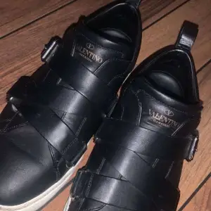 Snygga svarta sneakers från Valentino i skinn med coola remdetaljer. Perfekta för en stilren look, både till vardags och fest. De har en vit sula som ger en snygg kontrast till det svarta lädret.