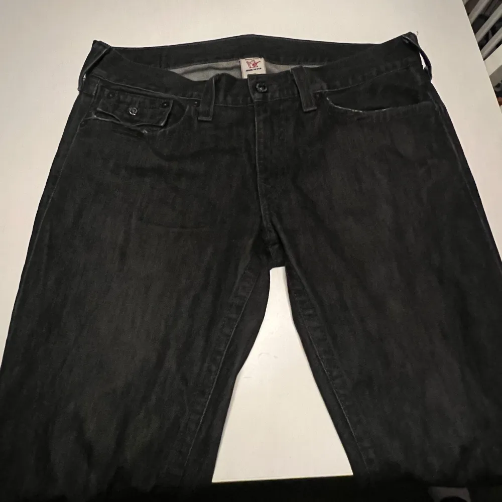 Säljer ett par svarta jeans från True Religion i bra skick. De har en klassisk femficksdesign med snygga detaljer på bakfickorna och knappar. Perfekta för både vardag och fest! 🖤. Farkut & Housut.