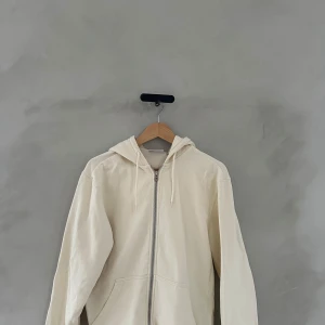 Beige hoodie med dragkedja - Säljer en snygg beige hoodie med dragkedja framtill. Den har en avslappnad passform och är perfekt för både höst och vår. Huvan har snören för justering och det finns praktiska fickor på framsidan. Perfekt för en chill dag eller en promenad i parken.