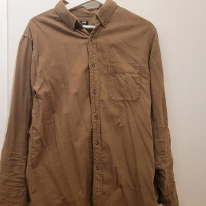 Brun skjorta från Uniqlo - Säljer en snygg brun skjorta från Uniqlo i storlek M. Skjortan är långärmad och har en klassisk krage med knappar hela vägen ner. Perfekt för höst och vår, och funkar både till vardags och lite finare tillfällen. Den har en bröstficka som ger en extra touch. 🧡