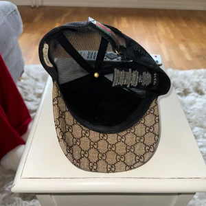 Äkta Gucci keps med bi-motiv - Snygg Gucci keps med det klassiska GG-mönstret i beige och brunt. Baksidan är i svart mesh för bra ventilation och justerbar rem med gröna och röda detaljer. Kepsen är såklart äkta.(Ser att det ligger en hel del fejk ute här så watch out) Använd men i okej skick. Sällsynt, går ej att köpa längre bara begagnad. 
