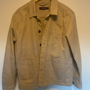 Beige overshirt från J.Lindeberg - Säljer en snygg beige overshirt från J. Den har en klassisk krage med knappar framtill. Materialet känns slitstarkt och bekvämt. Passar både till vardags och lite finare tillfällen. Storlek L och passar dig som är runt 185cm.