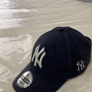 Mörkblå New York Yankees keps - Säljer en snygg mörkblå keps från New York Yankees. Kepsen har en broderad logga framtill och justerbar snapback-stängning. Perfekt för både vardag och sportiga tillfällen. Den är i nytt skick och redo att bäras med stil!