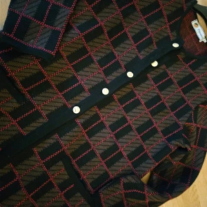 Rutig kofta från Missoni - Säljer en snygg lång rutig kofta från Busnel i svart, brunt och rött. Den har långa ärmar och knäpps med knappar framtill. Perfekt för höst och vinter, och den är i mycket bra skick. Passar både till vardags och fest! Passar stl 42-44 