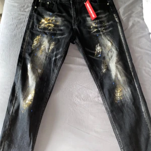 Svarta jeans med färgstänk - Coola svarta jeans med unika färgstänk i gult och blått. De har en sliten look med detaljer som ger en edgy stil. Perfekta för en avslappnad och trendig outfit. Passar bra till sneakers eller boots!