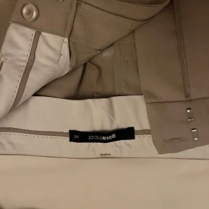 Beige kostymbyxor från Gina Tricot - Säljer ett par stiliga beige kostymbyxor från Gina Tricot i storlek XS. Byxorna har en klassisk design med hög midja och raka ben. Perfekta för både kontoret och festligare tillfällen. De är i mycket bra skick och har en snygg passform. Passa på att fynda dessa eleganta byxor!