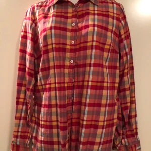 Rutig skjorta från Tommy Hilfiger - Säljer en superfin rutig skjorta från Tommy Hilfiger i rött, gult och blått. Skjortan har långa ärmar och knappar framtill. Perfekt för både vardag och fest! Den är i storlek 10 och har en skön passform. Passar perfekt till jeans eller chinos för en avslappnad look.