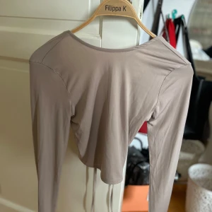 Beige långärmad topp med öppen rygg - Säljer en superfin beige långärmad topp. Den har en snygg öppen rygg med knytband och är perfekt för både vardag och fest. Toppen är i ett mjukt och stretchigt material som sitter skönt på kroppen.