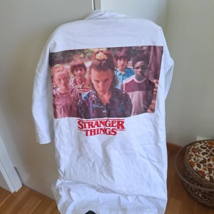 Vit Stranger Things tröja från Pull&Bear - Säljer en vit Stranger Things tröja från Pull&Bear. Den har ett stort tryck på baksidan med karaktärer från serien och texten 'Stranger Things' i rött. Perfekt för fans av serien! Tröjan är i bra skick och passar perfekt för en avslappnad stil.