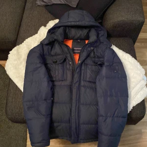Tommy Hilfiger puffer jacka - Mörkblå dun pufferjacka från Tommy Hilfiger. Huvan avtagbar, samt går att knäppa framtill. Inga hål, inga revor… Den är använd 3-4 vintrar, men fortfarande fräsch!!