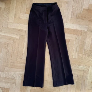 Stockholm Surfboard Club tailored pant s.36 - Beskrivning fr deras hemsida : - Relaxed bootcut fit - Full length - Slant pockets with hidden zip pocket - Press folds - Stockholm Surfboard Club flag label - Zip and hook-and-bar closure I gott skick! Använd ett fåtal gånger  