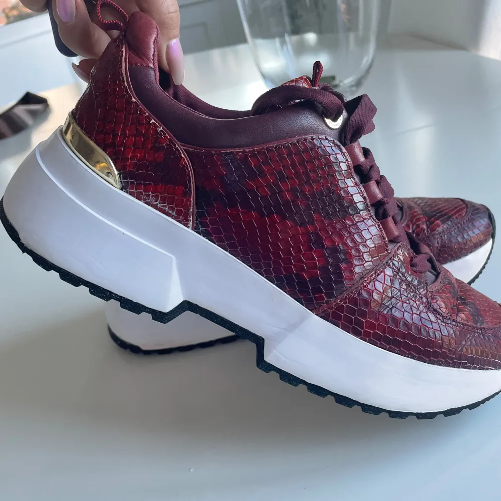 Sneakers i vinröd snakeskinn från Michael kors. Guldiga detaljer. Använda men i fint skick, nyputsade. Något slitage på gulddetaljerna se bild . Skor.