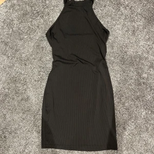 Svart ribbad klänning - Säljer en stilren svart ribbad klänning. Den är ärmlös och har en tight passform som framhäver figuren. Perfekt för en utekväll eller fest! Materialet är mjukt och stretchigt för extra komfort. Öppen rygg!