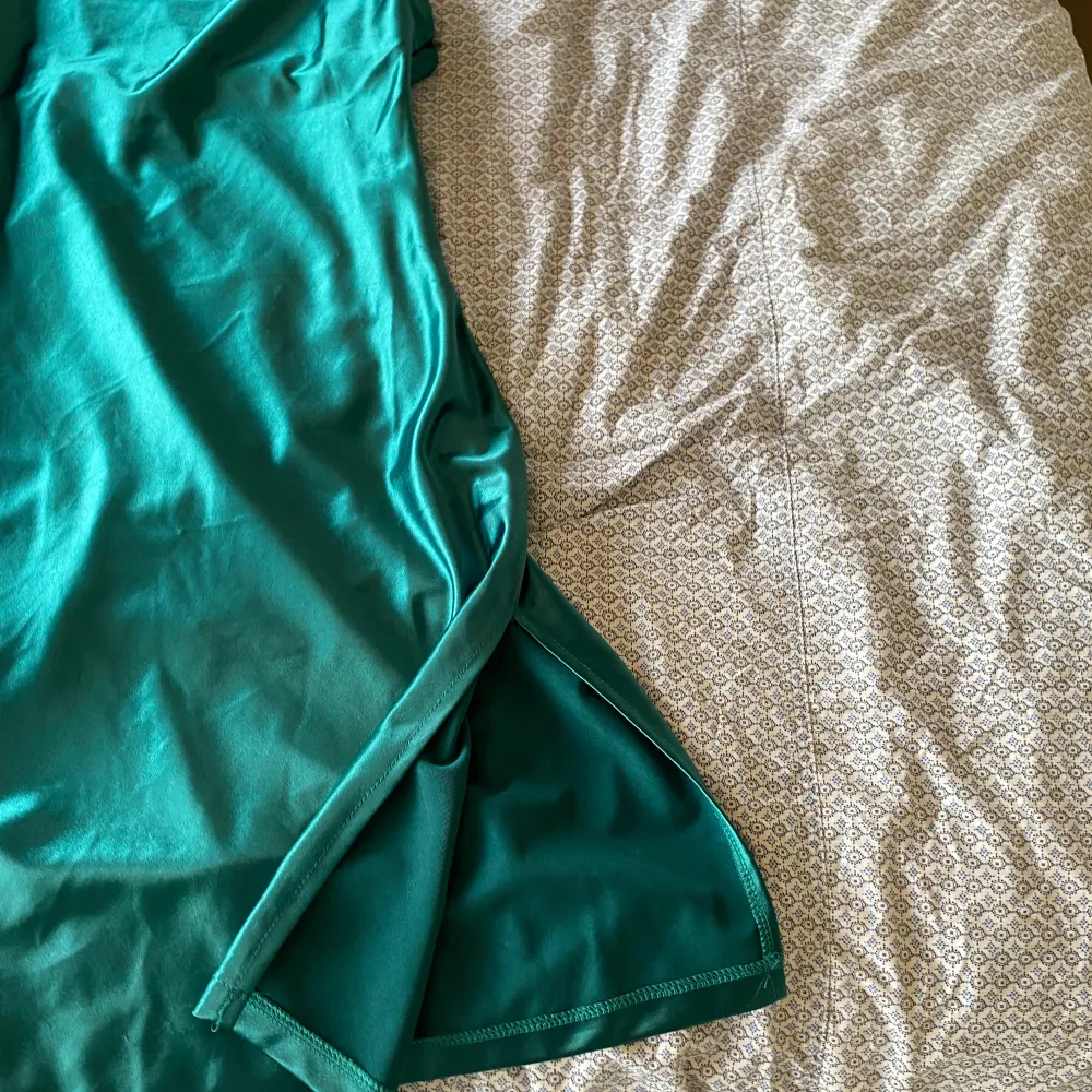 Säljer en elegant grön klänning i sidenmaterial. Den har en smickrande passform med smala axelband och en liten slits på sidan. Perfekt för festliga tillfällen!. Mekot.