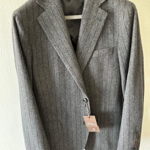 Oscar Jacobson Egel Blazer -  Stl. 54, slim fit och liten i storlek, 70% ull 30 % polyester. Kavajen har inte använts. Samtliga prislappar/etiketter sitter kvar och fickor har inte sprättats upp. Grå med svarta ränder. 