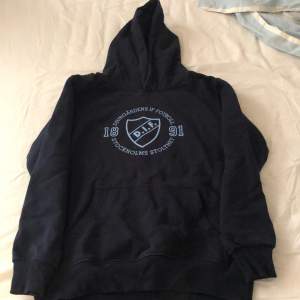 Säljer en svart hoodie med Djurgårdens IF Fotboll-logga på bröstet. Den har en stor ficka fram och en mysig huva. Perfekt för kalla dagar eller när du vill visa ditt stöd för laget!