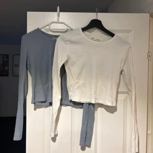 Två ribbade tröjor från Pull&Bear - Säljer två snygga ribbade tröjor från Pull&Bear i storlek M. Den ena är vit och den andra är ljusblå. Båda har långa ärmar och en croppad passform. Perfekta för en stilren och bekväm look.