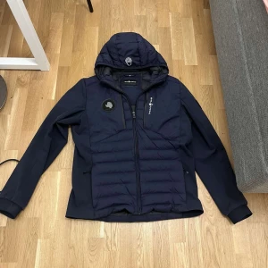 Mörkblå jacka från sail racing  - Snygg mörkblå jacka från sail racing med huva och dragkedja. Jackan har en quiltad design på framsidan och är långärmad. Perfekt för kyligare dagar. Kvitto och vid eventuella frågor skriv!!