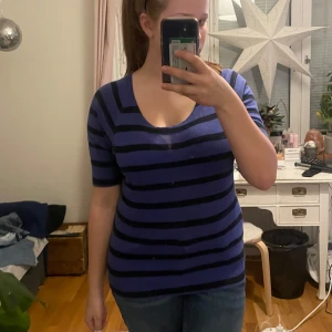 Blå och svart randig topp från Ann Taylor - Säljer en snygg lila och svart randig topp från Ann Taylor. Toppen har en rund halsringning och trekvartsärmar, perfekt för en stilren look. Passar bra till både jeans och kjol. Storleken har försvunnit från lappen som du ser, men jag skulle säga att den är M.