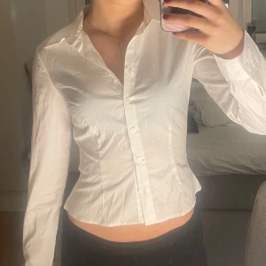 Vit skjorta med knappar - Snygg vit skjorta med en klassisk design och knappar framtill. Skjortan har en figurnära passform och långa ärmar, 