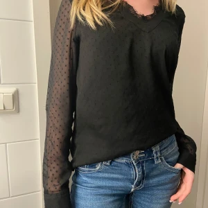 Svart blus med spetsdetaljer - Snygg svart blus med transparenta prickiga ärmar och spetskant vid halsringningen. Perfekt för en stilren look. Pris kan diskuteras💖