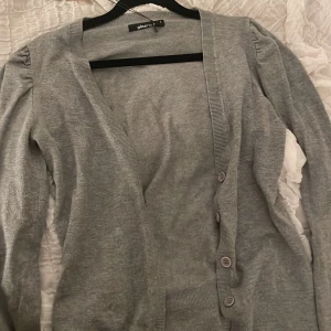 Grå kofta från Gina Tricot - Säljer en stilren grå kofta från Gina Tricot. Den har långa ärmar med lätt puff vid axlarna och knappar framtill. Skriv privat om ni har frågor 🫶🙏