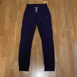 Mörkblå mjukisbyxor från GANT - Säljer ett par mörkblå mjukisbyxor från GANT med snörning i midjan och broderad logga på sidan. Perfekta för en avslappnad stil. Storlek 176 - 16 år