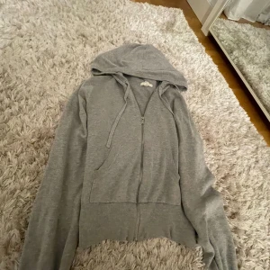 Stickad hoodie - Mysig grå hoodie med dragkedja och huva. Perfekt för kyliga dagar. Den har långa ärmar och en praktisk ficka framtill.