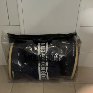 Blå Moon Boots med snörning - Säljer ett par OANVÄNDA klassiska blå Moon Boots med vit text och snörning. Perfekta för kalla vinterdagar med sin varma och vadderade design. De har en robust sula och är lätta att ta på och av.