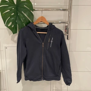 Mörkblå hoodie från Sail Racing - Snygg mörkblå hoodie från Sail Racing med dragkedja och huva. Perfekt för kyliga dagar med sitt stilrena utseende och bekväma passform.