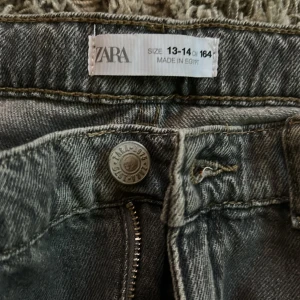Grå jeans från Zara - Säljer ett par grå jeans från Zara i storlek 164. De har en klassisk design med dragkedja och knapp framtill. Perfekta för en avslappnad stil. Nypris 499:-