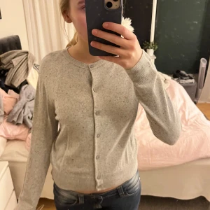 Grå kofta med knappar - Säljer en stilren grå kofta med knappar framtill. Koftan har långa ärmar och en rund halsringning, perfekt för lager-på-lager-stil. Passar bra till både jeans och kjol. Skriv om ni har några frågor!💞