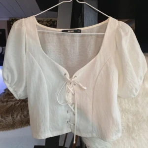 Vit blus från Bik Bok - Säljer en söt vit blus från Bik Bok med korta puffärmar och snörning framtill. Perfekt för en somrig look!