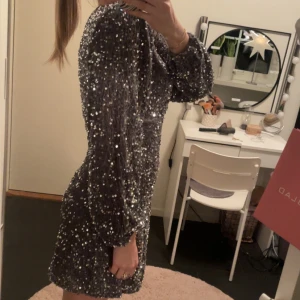Glittrig silverklänning - Snygg glittrig silverklänning med v-ringning och långa ärmar. Perfekt för en festlig kväll med sitt glittrande material och figurnära passform. Bara andvänd 1 gång😍